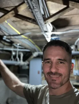 Frank Karichko beneath exposed basement plumbing