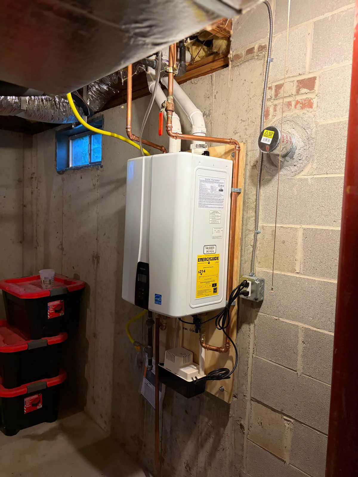 Wall-mounted tankless water heater with copper connections in a basement utility area