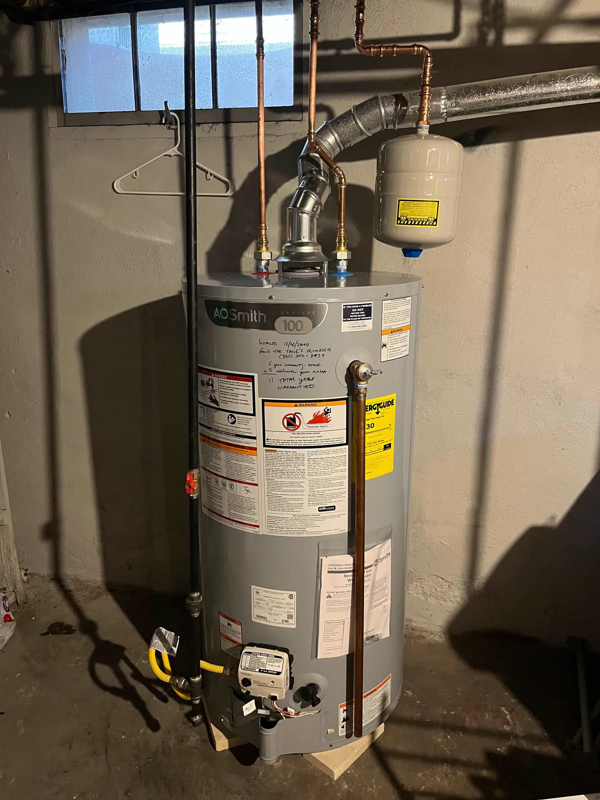 Tank water heater with copper piping, a metal vent, and an expansion tank in a basement